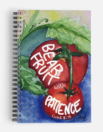 A spiral-bound notebook featuring a watercolor-style illustration of red tomatoes on the cover with the words 'BEAR FRUIT with PATIENCE LUKE 8:15' written in white script.