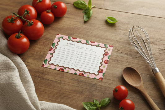 A recipe card template with a scalloped brown border on a pink background decorated with red tomatoes and green herbs. The card includes fields for recipe title, prep time, cook time, serves, and two columns of writing lines.